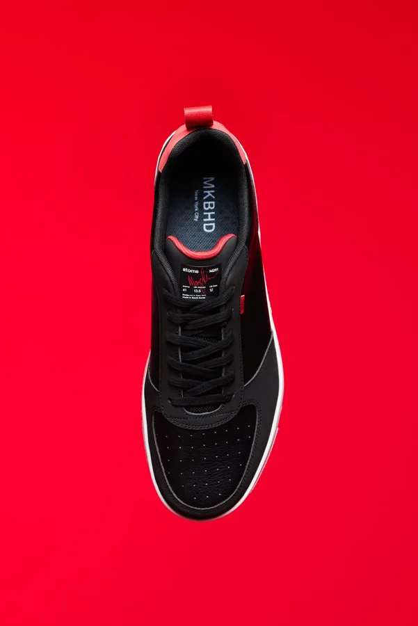 Top-down product photograph of a black Atoms x MKBHD sneaker on a vivid red background